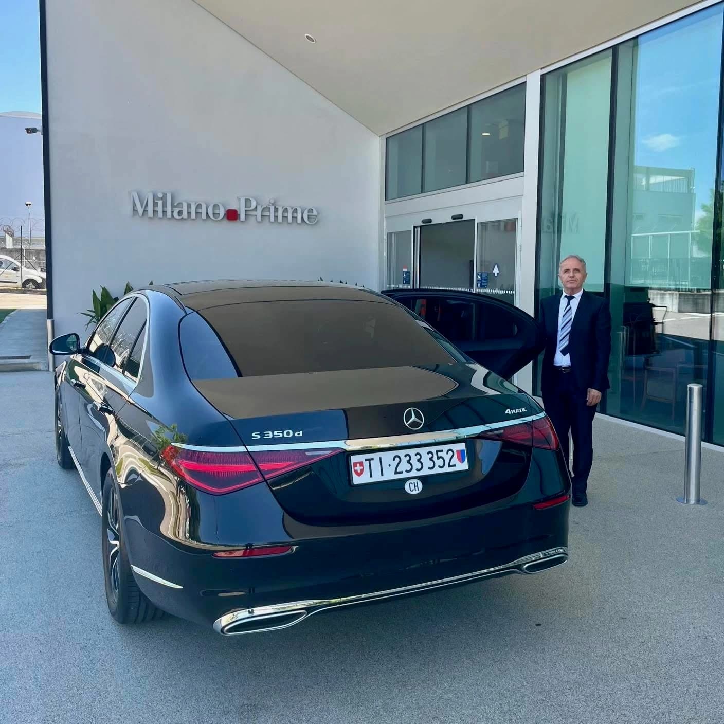 Professional chauffeur in a dark suit beside a black Mercedes-Benz S-Class, a luxury sedan